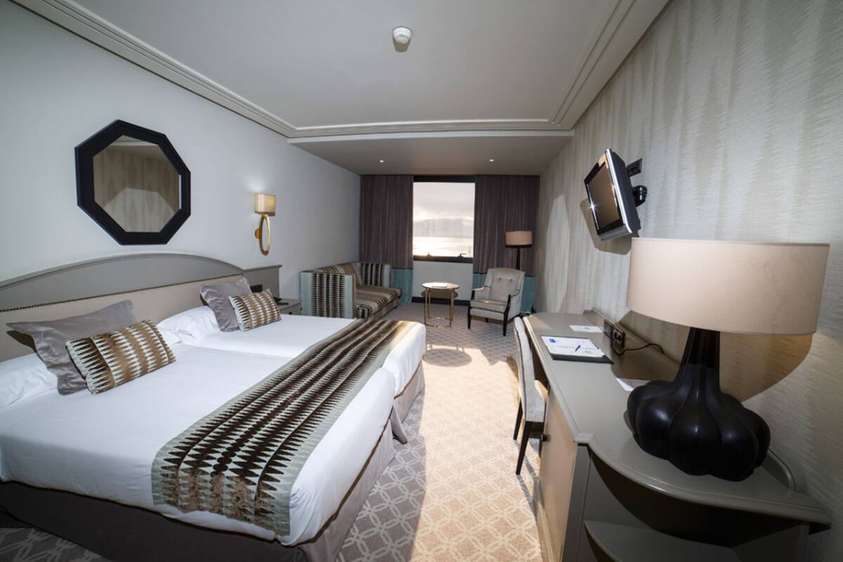 Habitación de hotel con dos camas, un escritorio, una silla, un televisor y una ventana con cortinas.