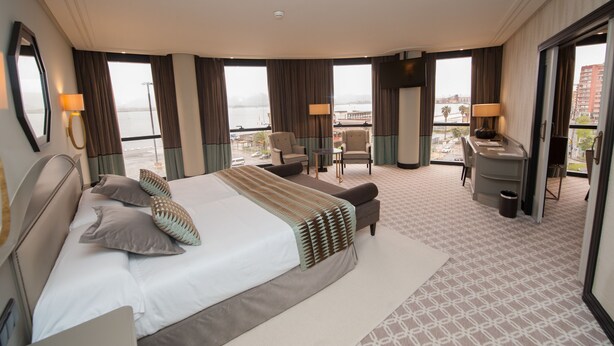 Habitación de hotel con una cama grande, dos sillones, un escritorio y vistas a la ciudad.