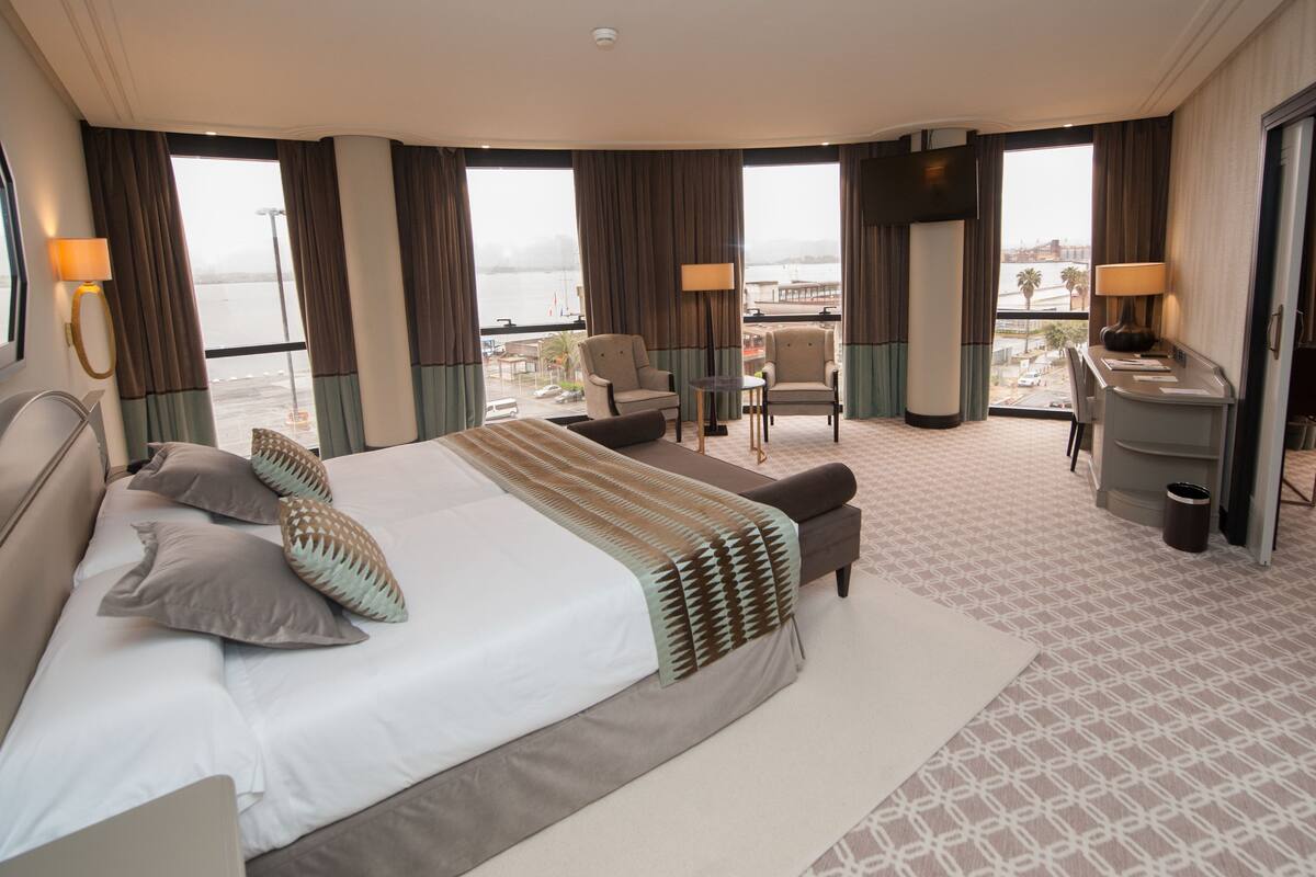 Habitación de hotel con una cama grande, dos sillones, un escritorio y vistas a la ciudad.