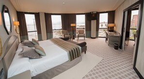 Une chambre d’hôtel avec un grand lit, deux fauteuils, un bureau et une vue sur le paysage urbain.