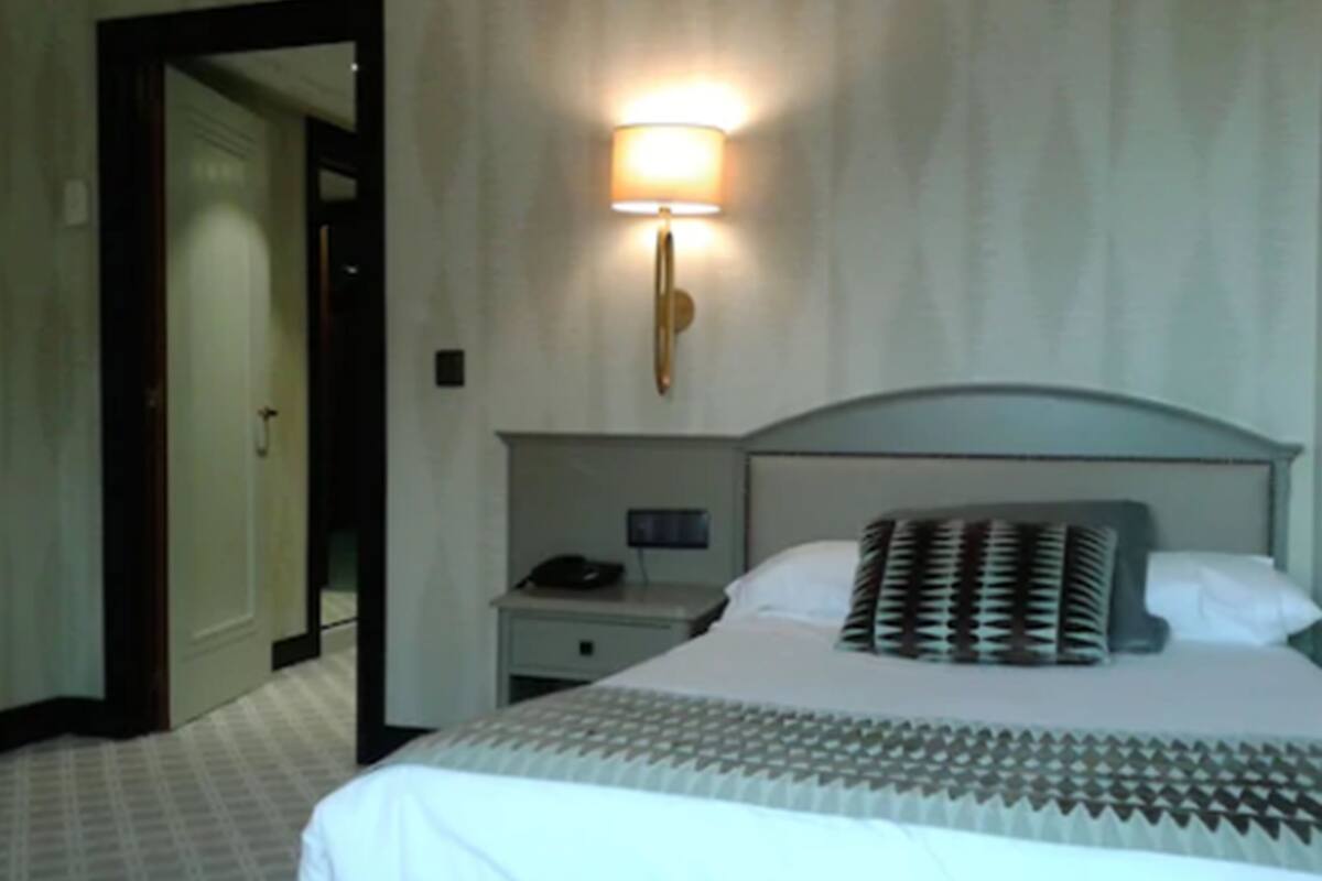 Una habitación de hotel con una cama, una mesita de noche, una lámpara y un espejo.
