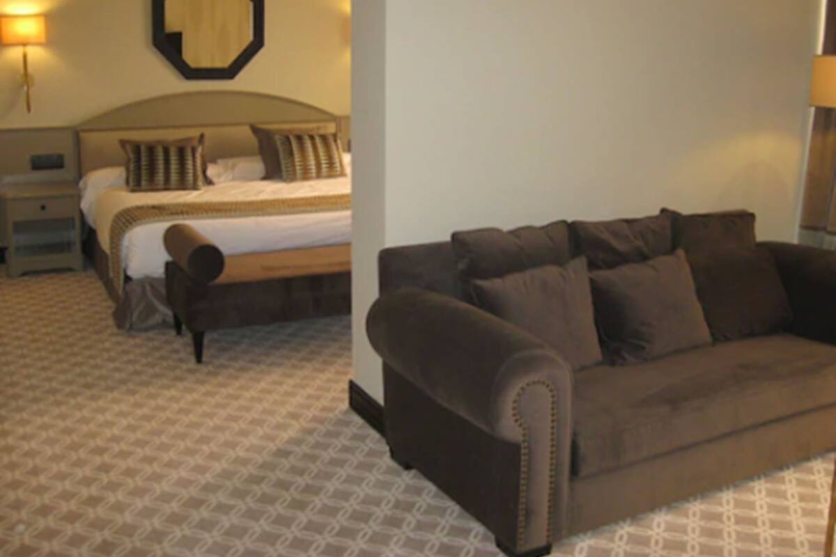Una habitación de hotel con cama, mesita de noche, lámpara, sofá y espejo en la pared.