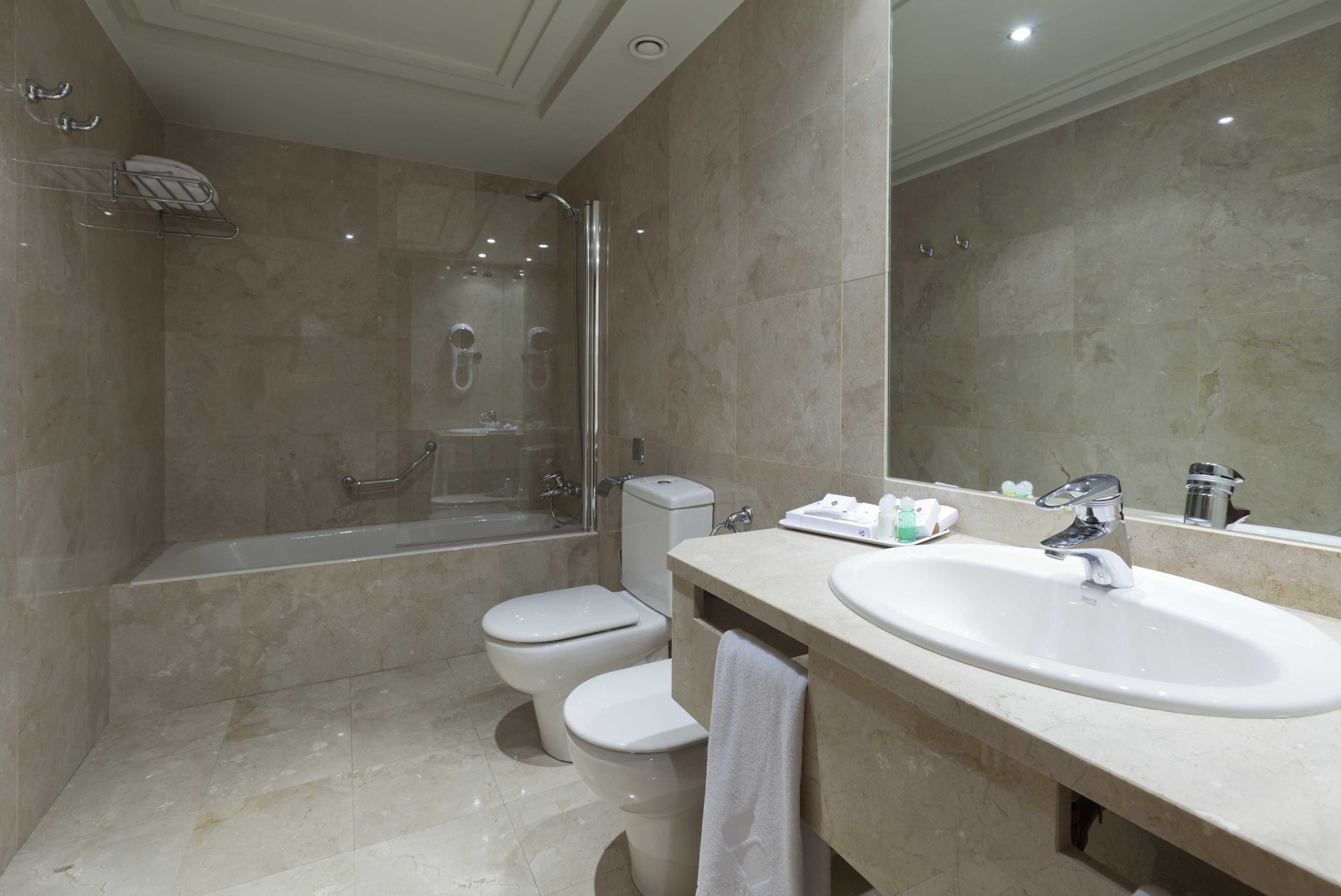 Une salle de bain moderne avec une douche à parois de verre, deux toilettes, un lavabo et un miroir.