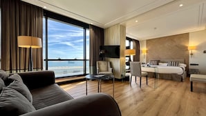 Habitación de hotel con un ventanal amplio que ofrece vista al mar, una cama, un escritorio y un sofá.