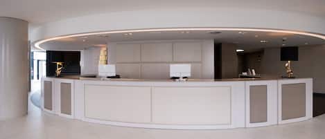 A modern reception desk with a curved design, a large padded back, and two lamps.