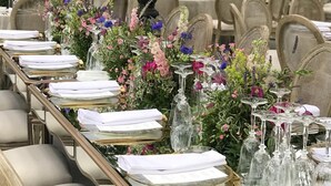 Una larga mesa de comedor decorada con servilletas blancas, cristalería transparente y centros de mesa florales.