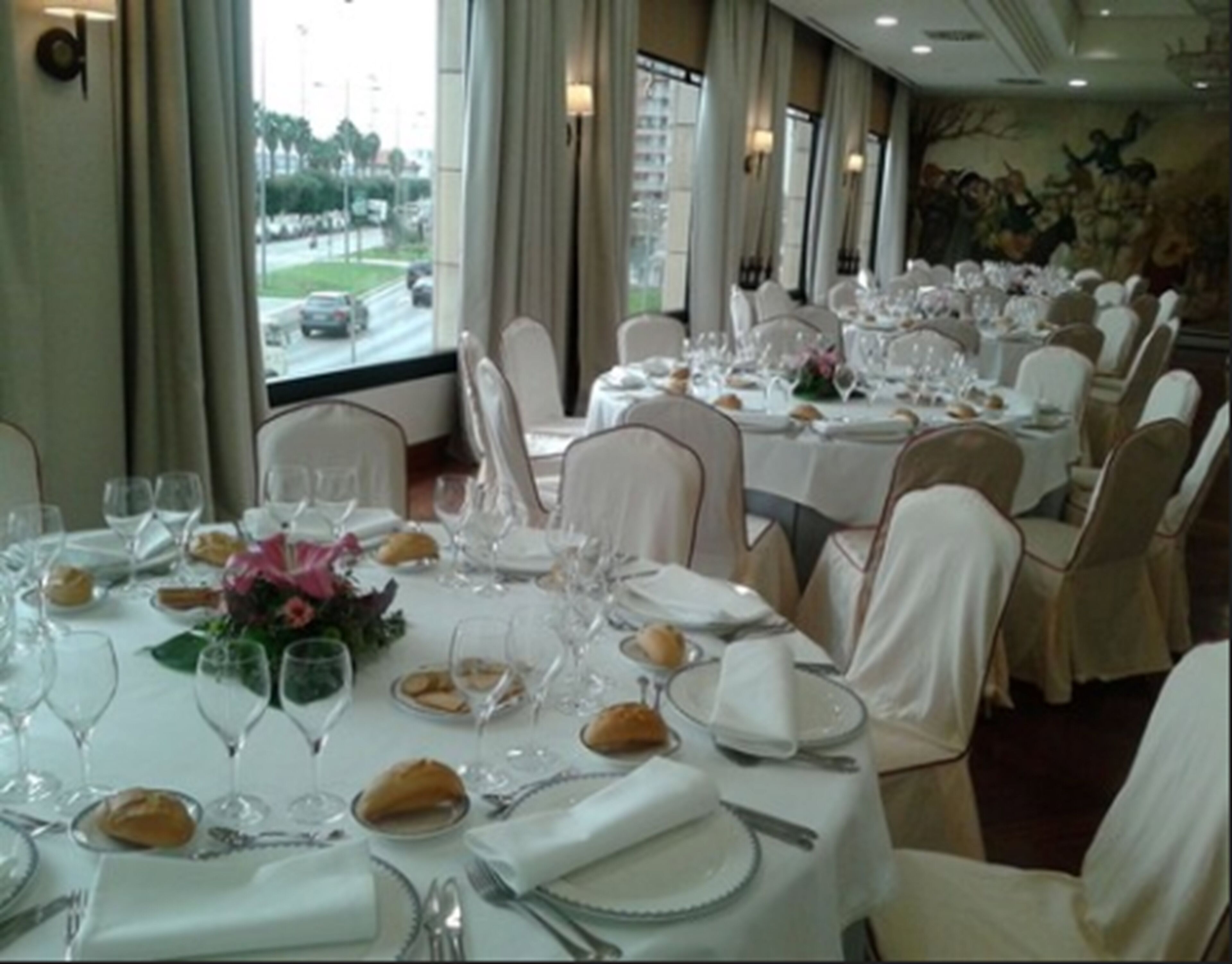 A banquet hall with round tables set for dining, each with white tablecloths, glassware, and folded napkins.
