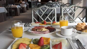 Una mesa de desayuno con platos de fruta, pastelería y vasos de zumo.