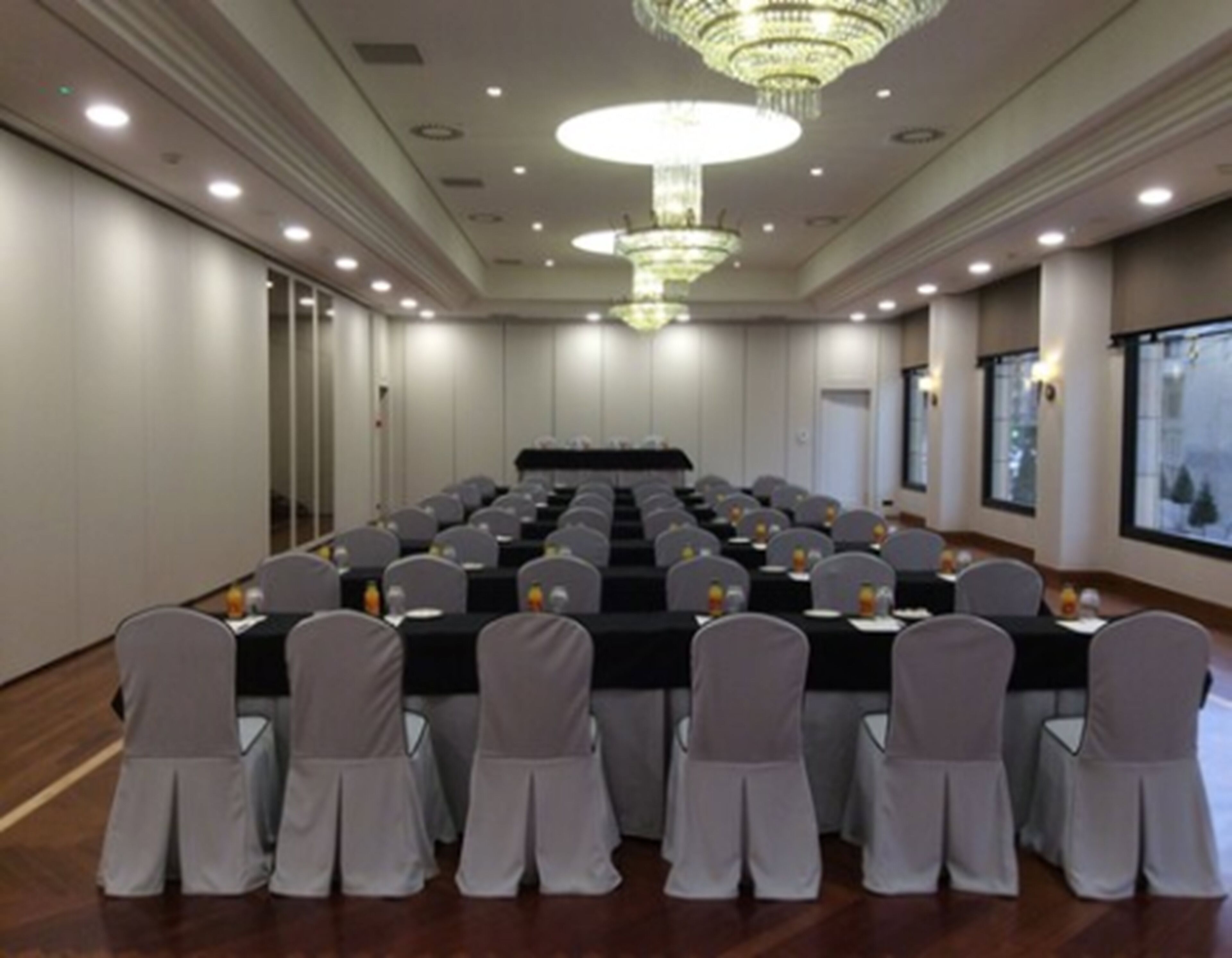 Uma sala de conferências com mesas e cadeiras dispostas em fileiras, um candelabro e grandes janelas.