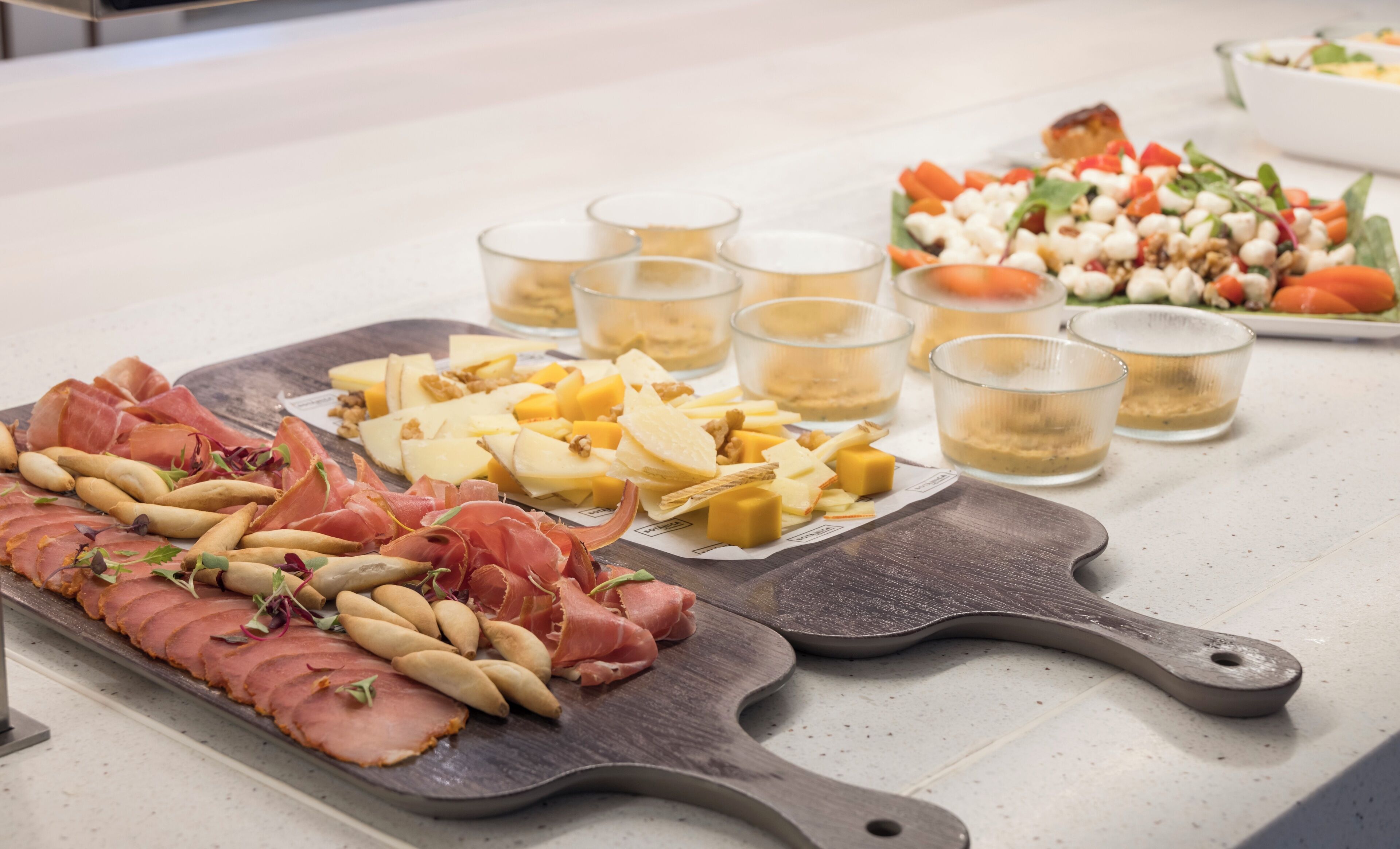 A charcuterie board with various meats, cheeses, and nuts, accompanied by small glasses of a beverage.