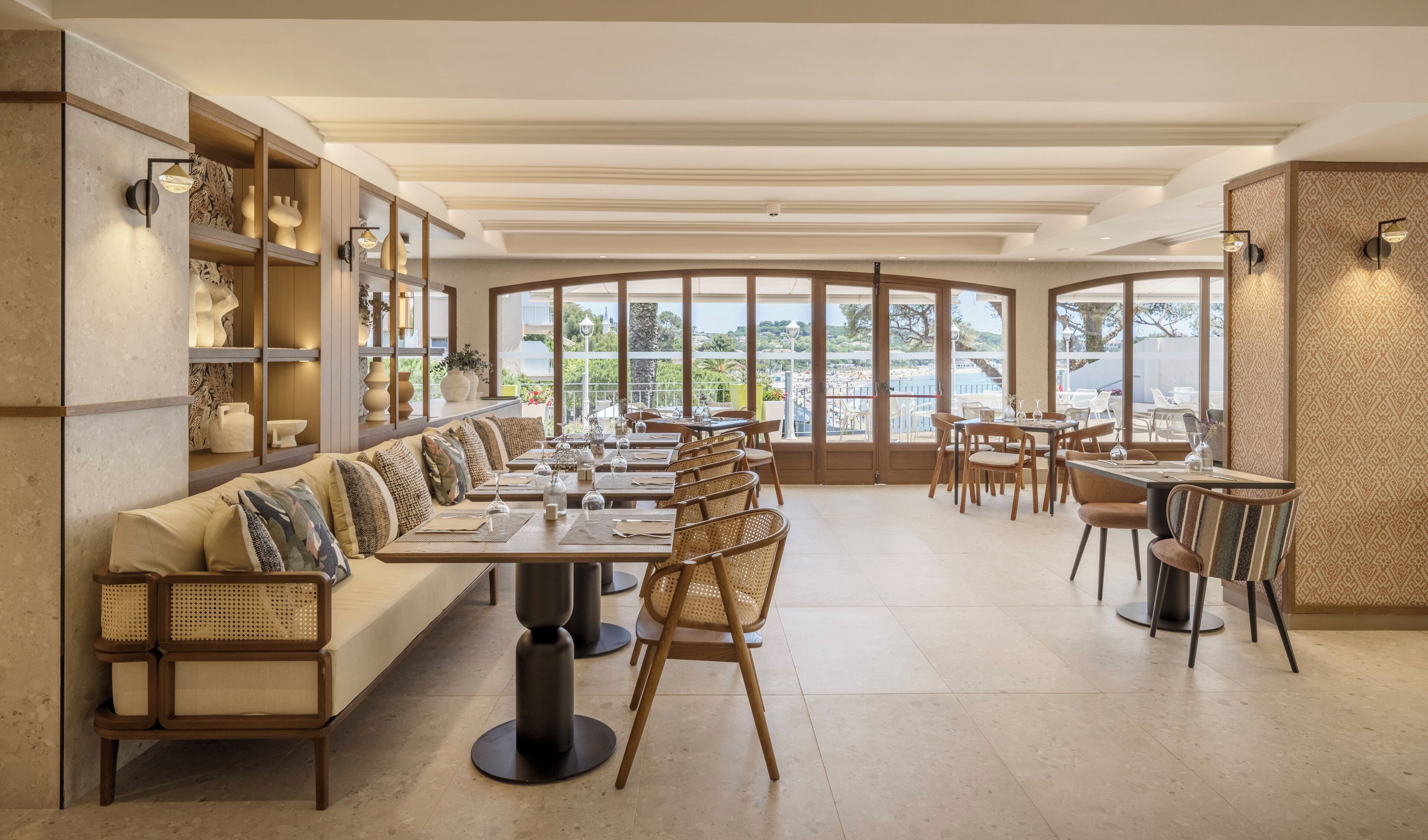 A restaurant with a long counter, cushioned seating, and large windows offering a view of the outdoors.