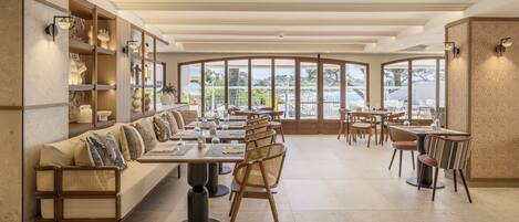 A restaurant with a long counter, cushioned seating, and large windows offering a view of the outdoors.