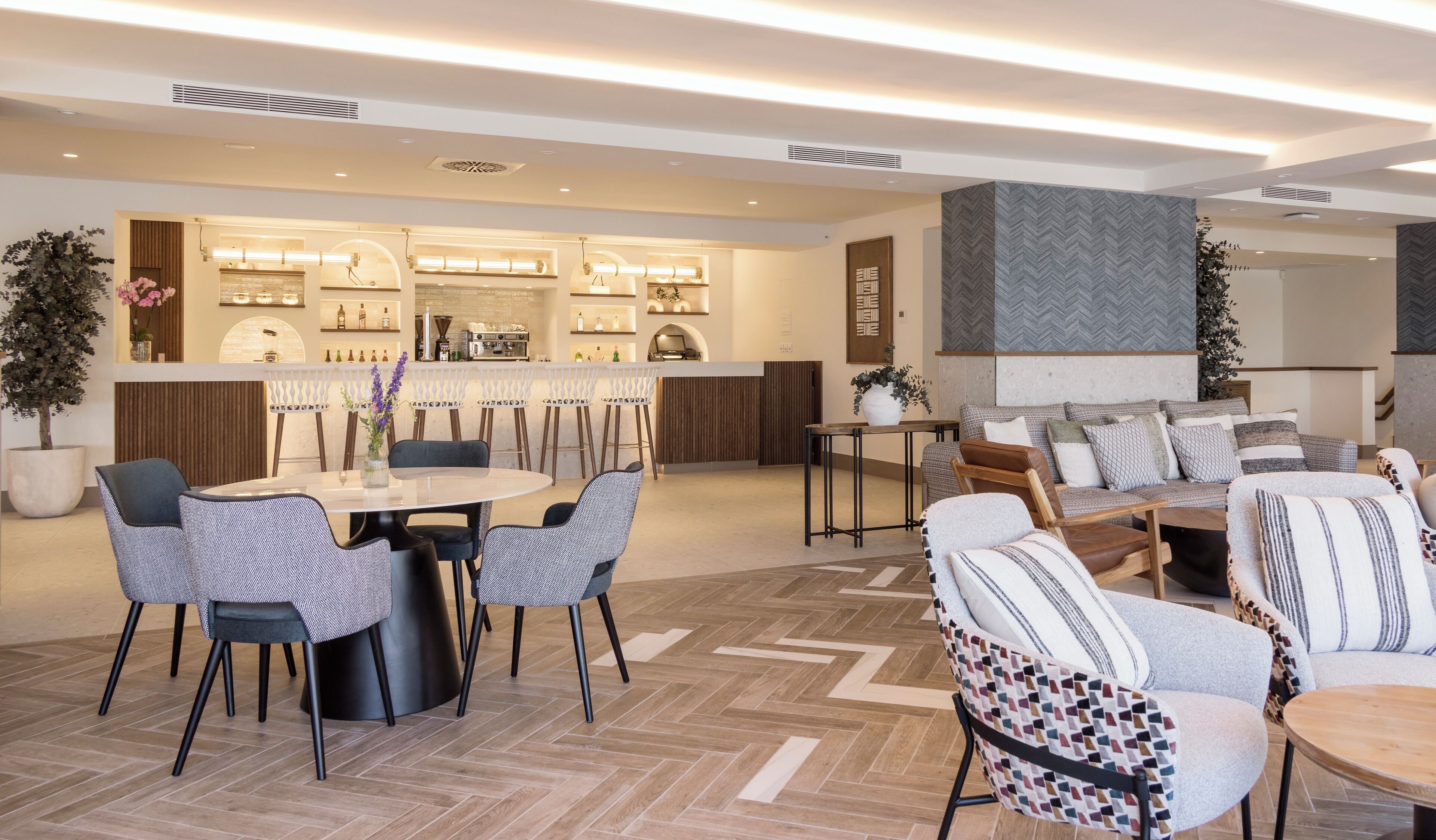 Un moderno vestíbulo de hotel con una zona de bar, arreglos de asientos y un suelo con estampado de espiga.