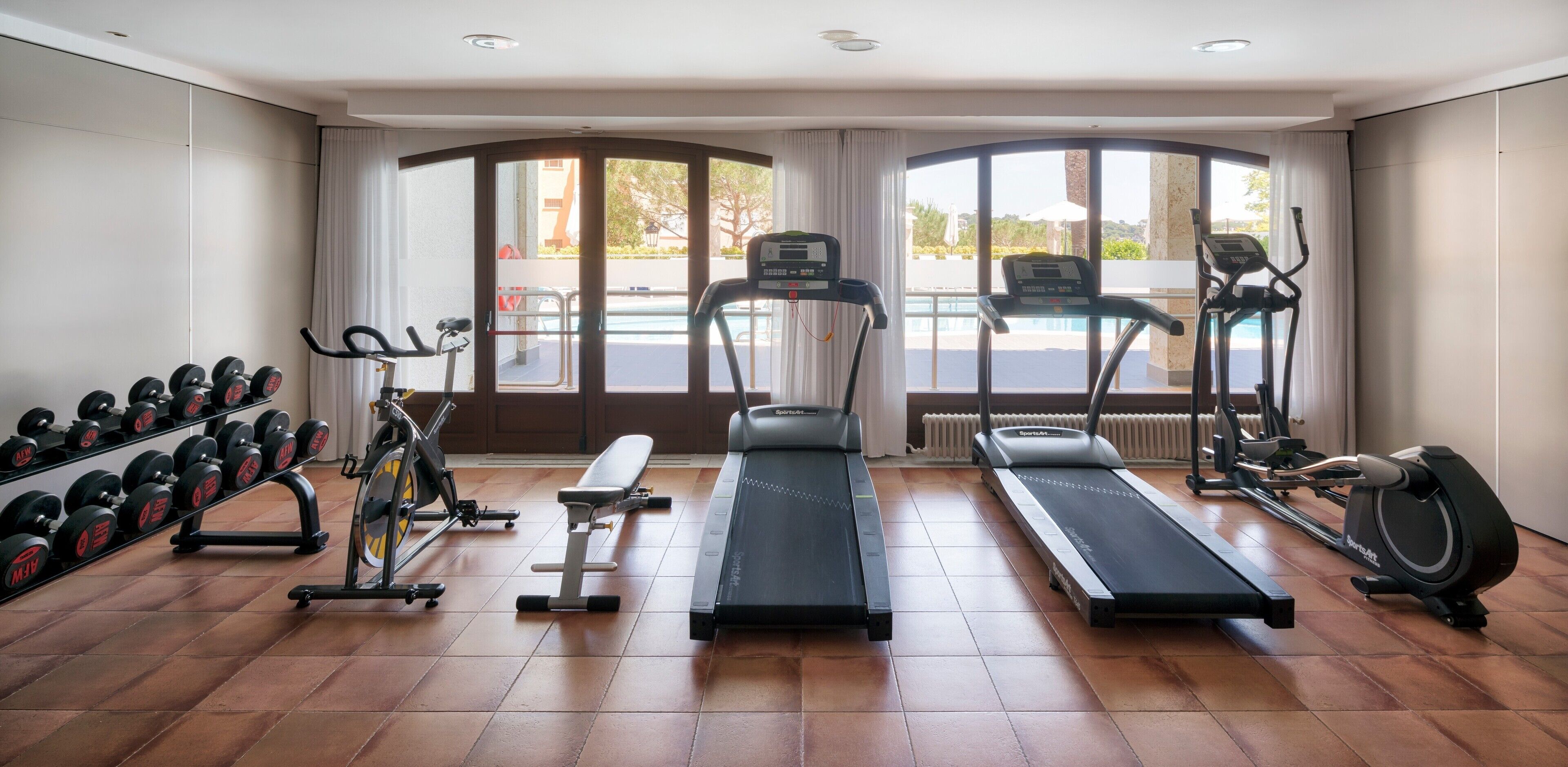 Une salle de sport équipée de tapis de course, d’un appareil elliptique, d’un banc de musculation et d’haltères.