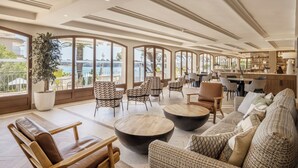 Un vaste espace de vie doté d’une grande fenêtre offrant une vue panoramique, aménagé avec des canapés en cuir, des fauteuils à motifs et une table basse centrale.