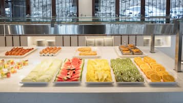Un buffet proposant une variété de fruits, de pâtisseries, et une rambarde en verre en arrière-plan.