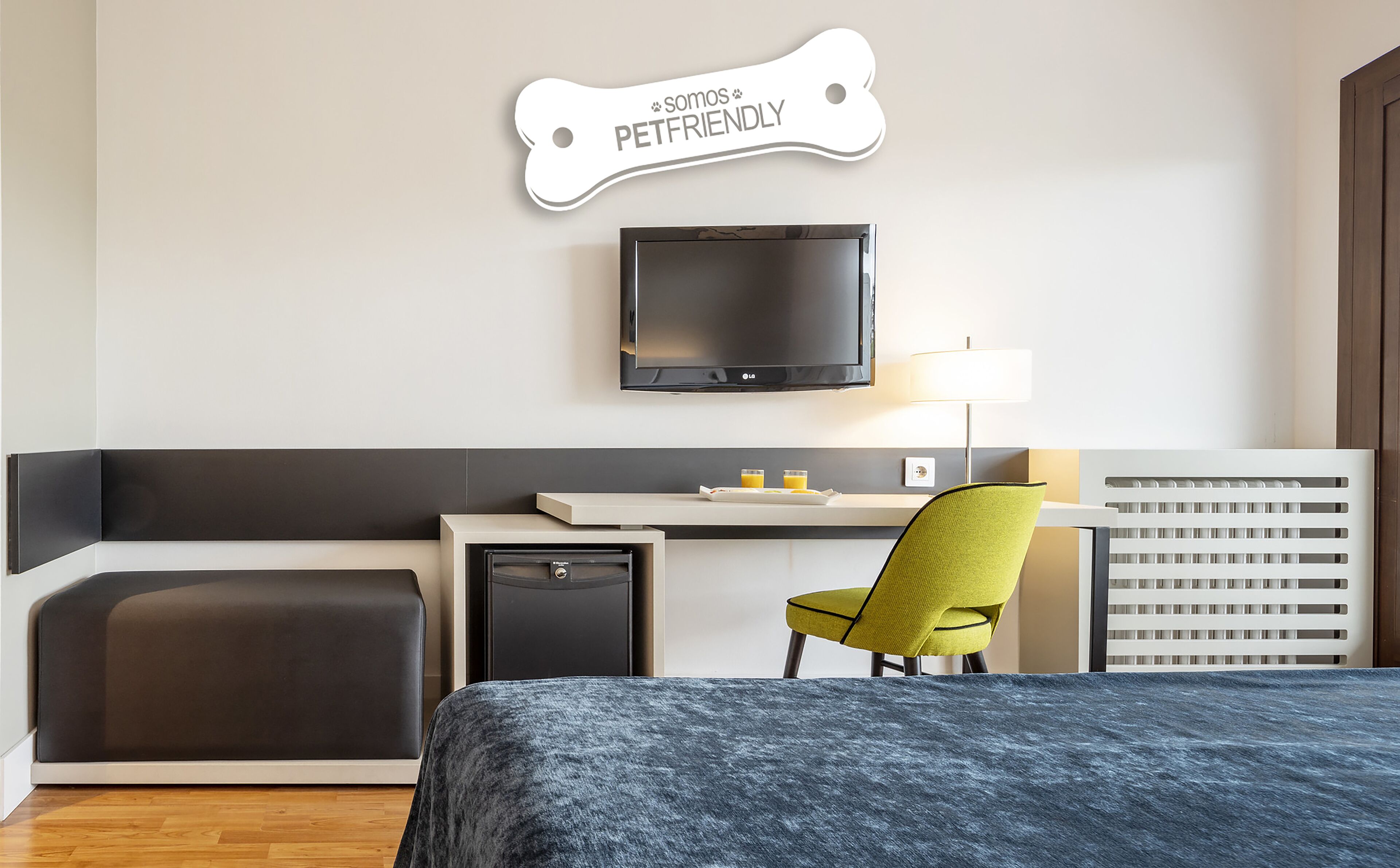 Habitación de hotel moderna con cama, escritorio con silla, televisión y un cartel que indica que el hotel admite mascotas.