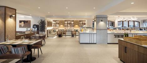 A modern hotel lobby with a central seating area, a coffee bar, and a buffet.