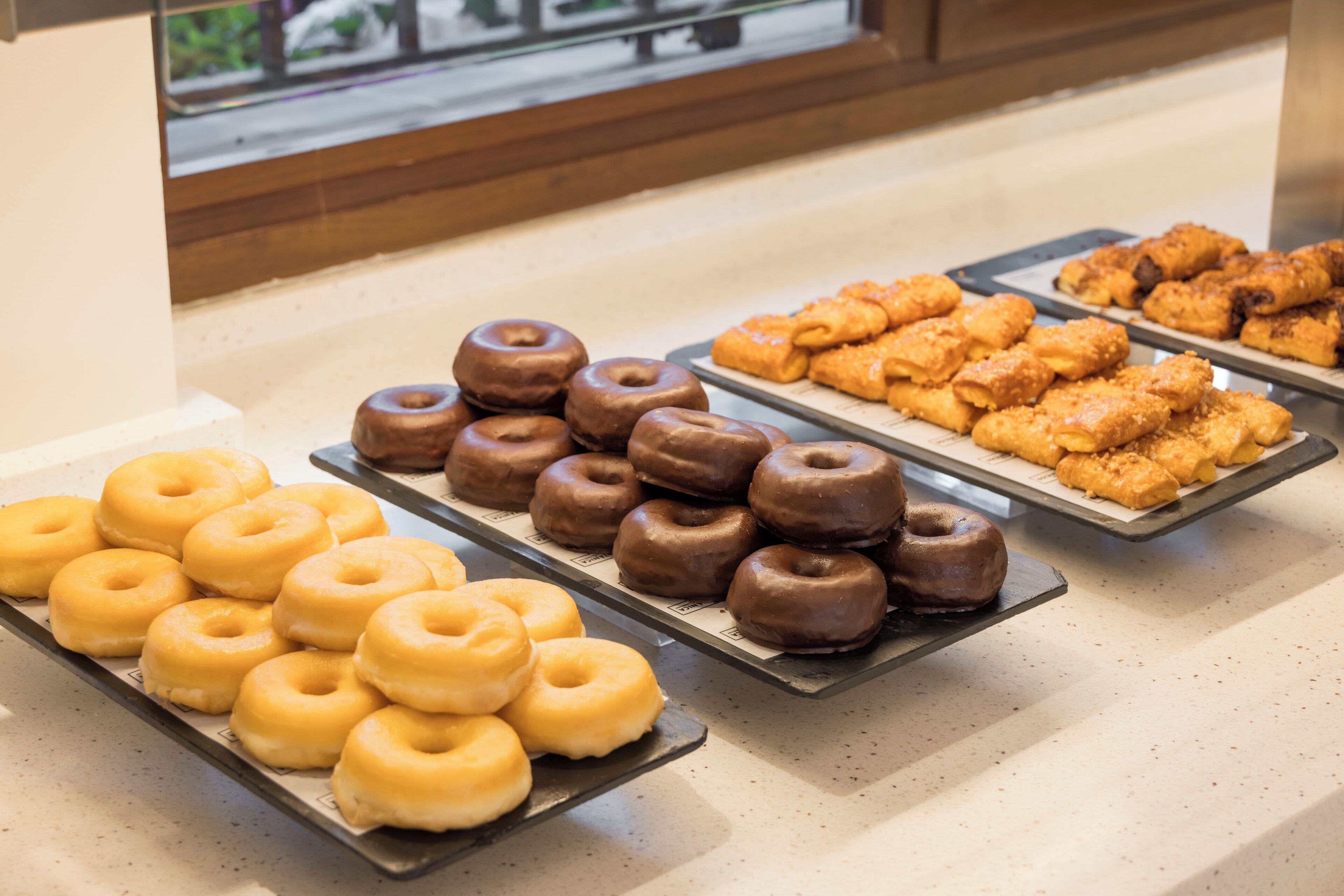 Des plateaux remplis de beignets et de viennoiseries sont exposés dans le rayon boulangerie.