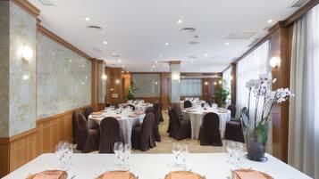 Una sala de banquets amb taules rodones preparades per dinar, equipada amb teles de taula blanques, plats, vasos i coberts.