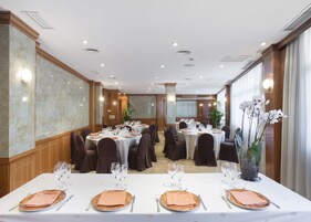 Salão de banquetes com mesas redondas preparadas para refeições, equipado com toalhas brancas, pratos, copos e talheres.