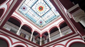 Een meerlaags atrium met een glazen koepel, witte en rode architectonische details en balkons met leuningen.