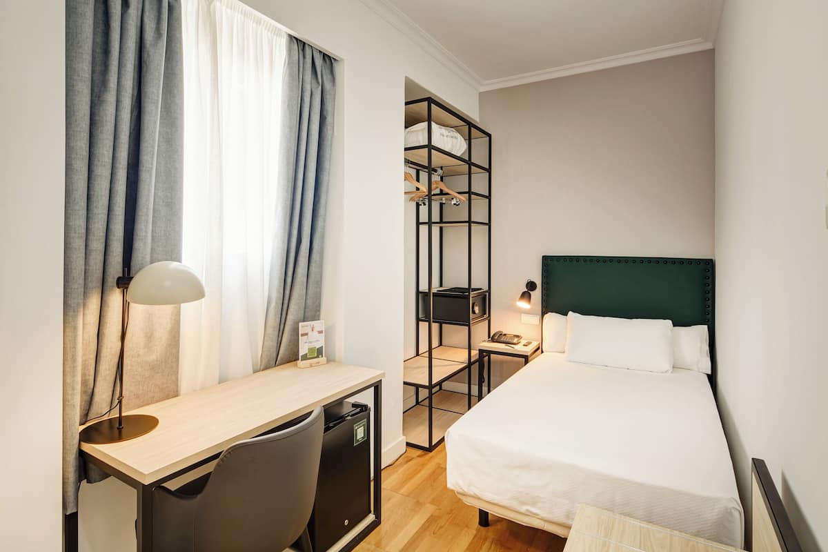 Ein Hotelzimmer mit Bett, Schreibtisch, Stuhl und Kleiderschrank.