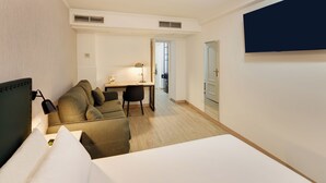 Een hotelkamer met een bed, een bank, een bureau, een stoel, een televisie en een deur naar een badkamer.