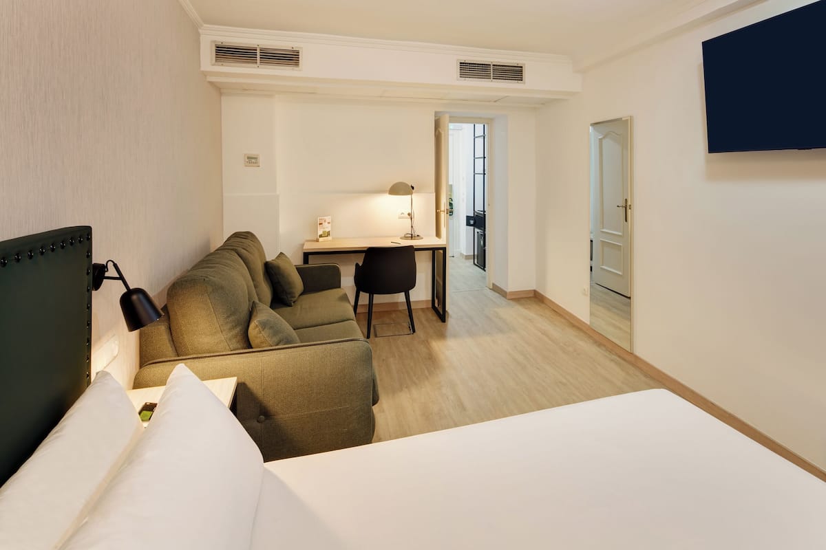 Ein Hotelzimmer mit Bett, Sofa, Schreibtisch, Sessel, Fernseher und einer Tür zum Badezimmer.