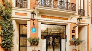 Het uiterlijk van Hotel Las Casas de los Mercaderes, met een duidelijke ingang, een bord dat aangeeft dat het een hotel is, en twee plantenbakken met planten op het trottoir.