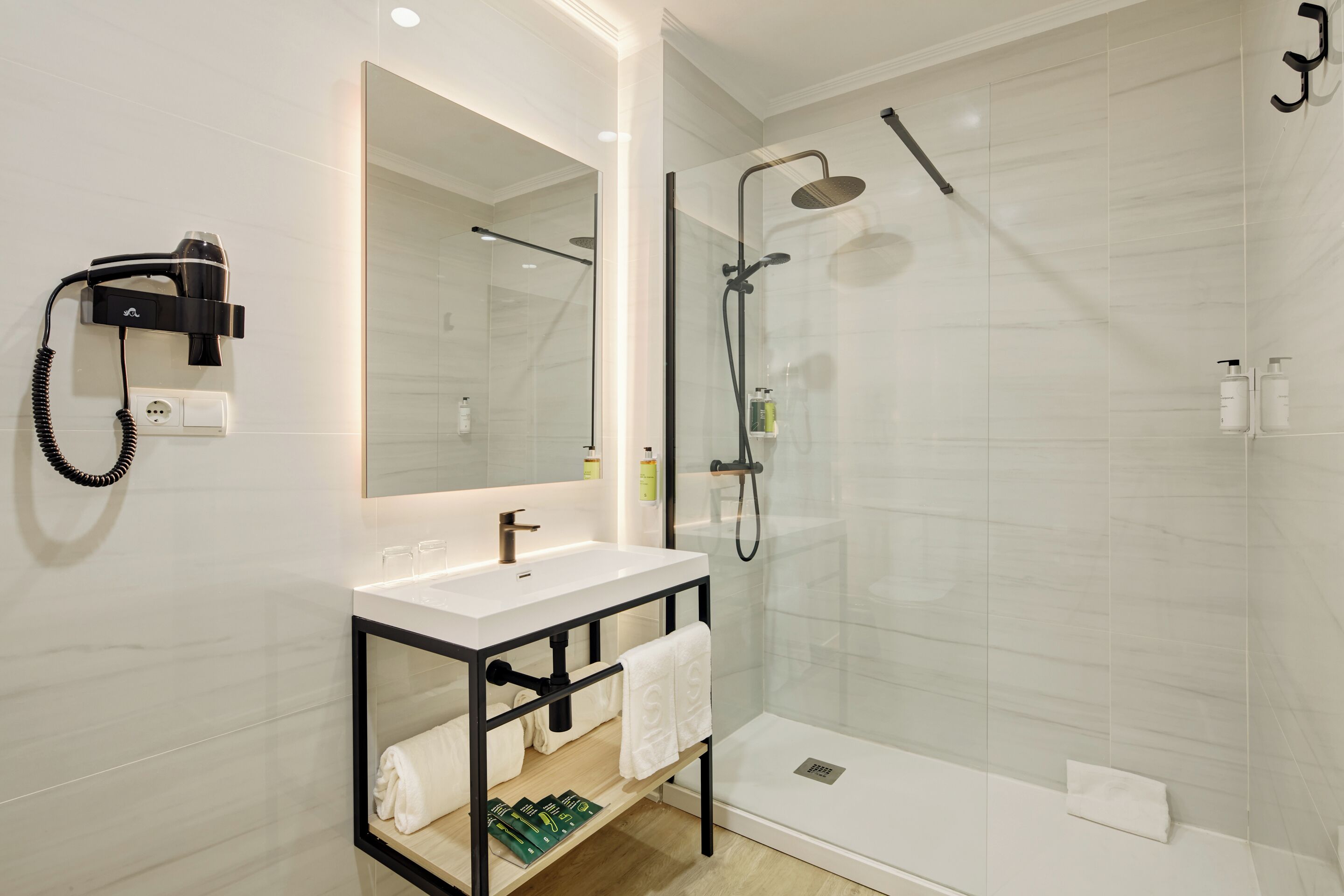 A modern bathroom with a white sink, a mirror, a hairdryer, and a glass-enclosed shower area.