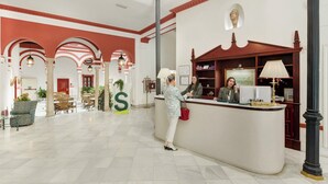 Een hotel receptie met een receptionist, een groot, S-vormig bord en een receptiebalie.