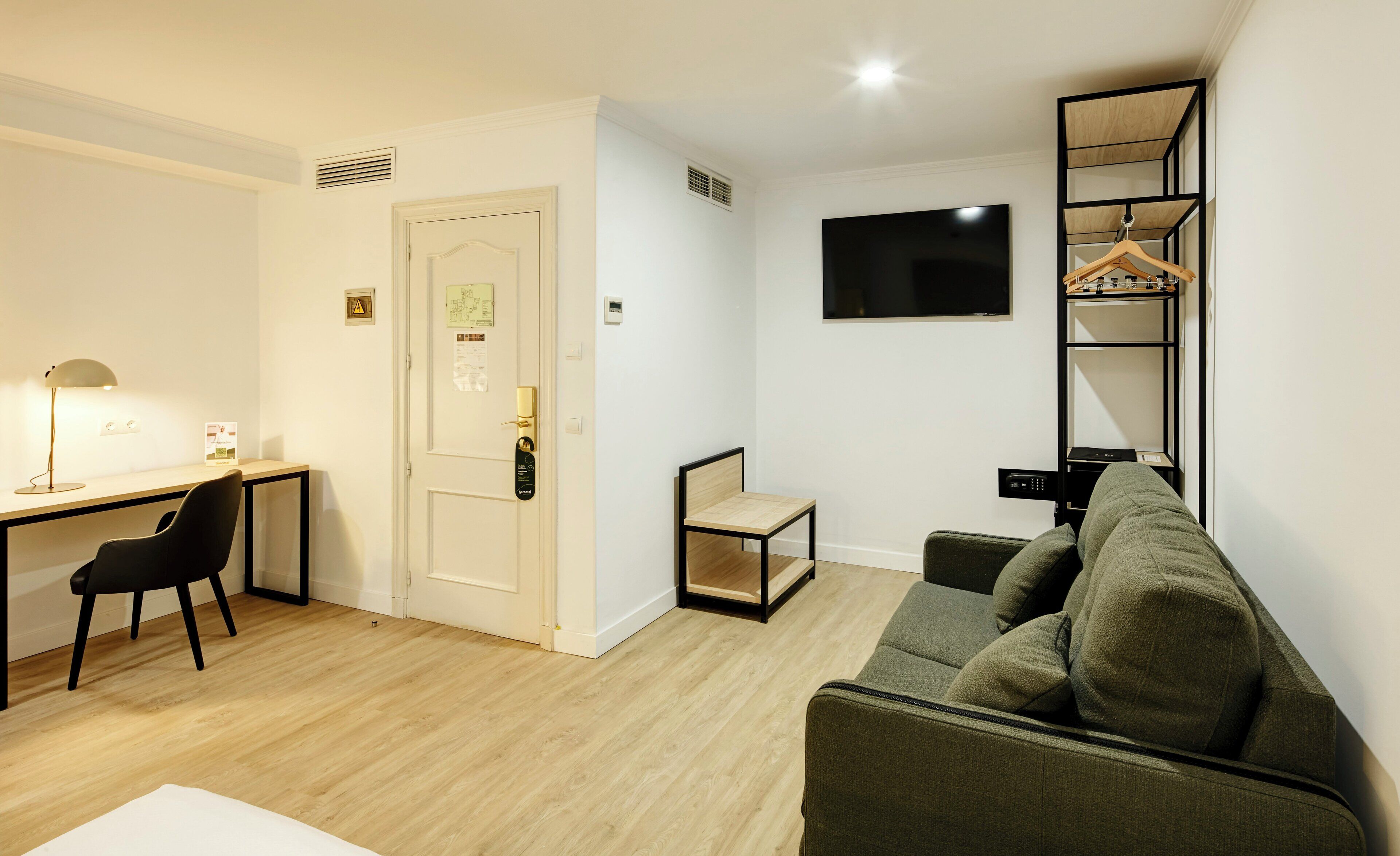 A modern living room with a desk, a chair, a sofa, and a TV mounted on the wall.