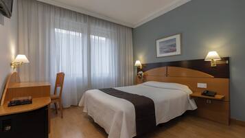 Habitación de hotel con cama, lámparas de noche, escritorio con silla, una mesita y un aparador.