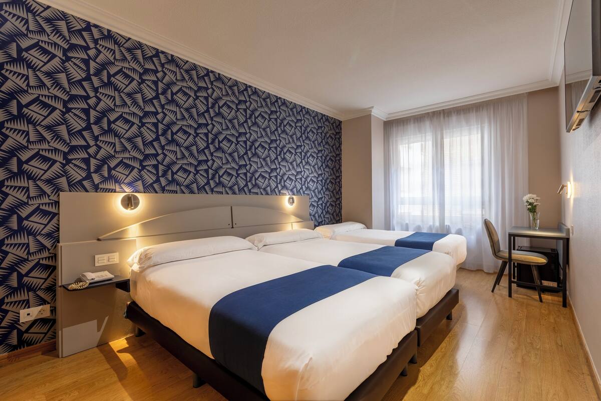 Habitación de hotel con dos camas, un escritorio y una pared con diseño.