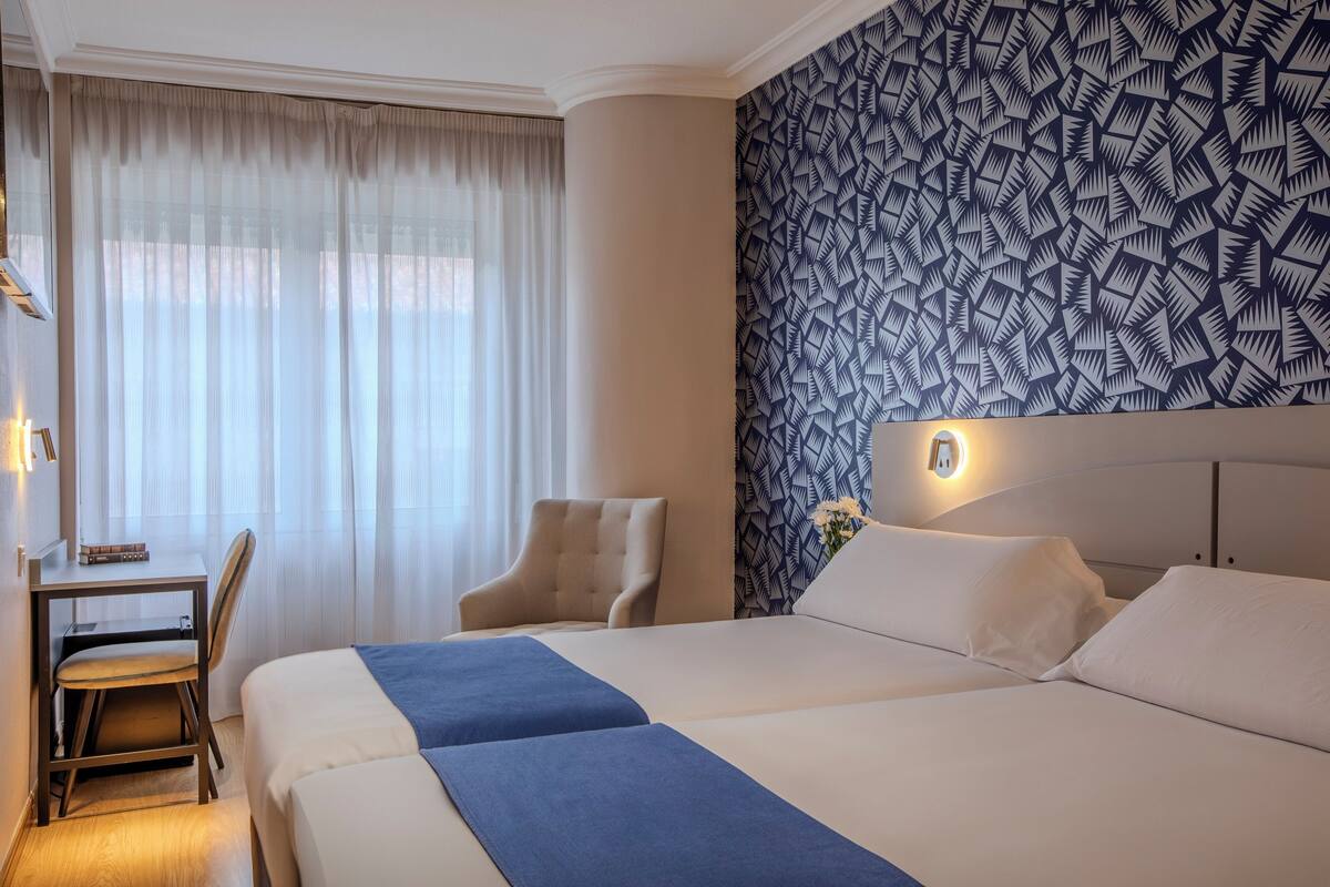 Una habitación de hotel con una cama grande, un escritorio con una silla y un papel tapiz estampado.
