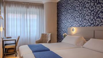 Una habitación de hotel con una cama grande, un escritorio con una silla y un papel tapiz estampado.