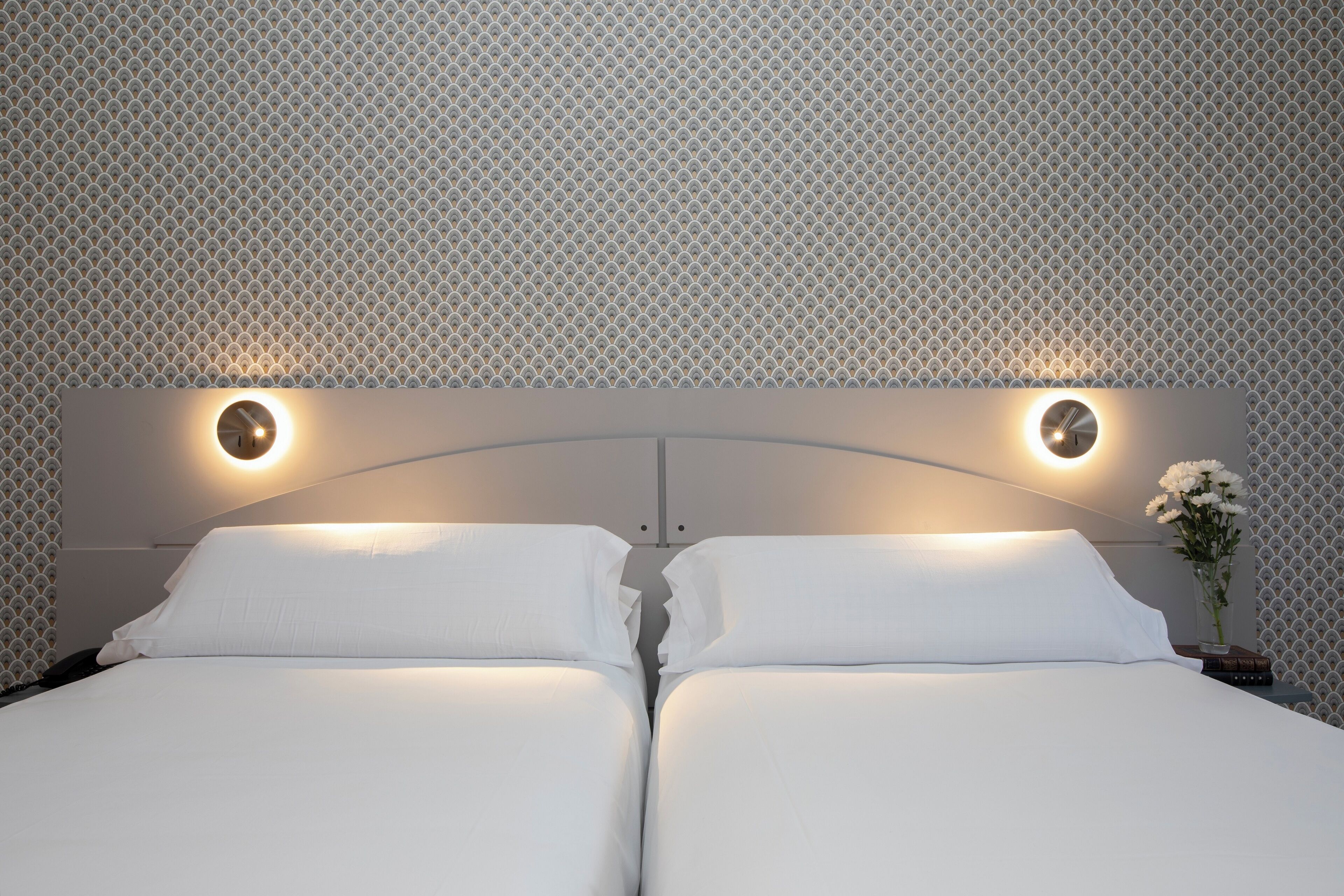 Una cama doble con dos mesitas de noche, cada una con una lámpara redonda fijada a la pared.