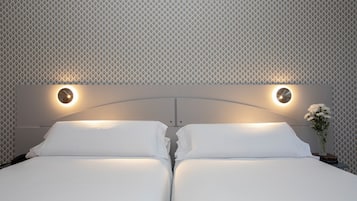 Una cama doble con dos mesitas de noche, cada una con una lámpara redonda fijada a la pared.
