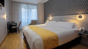 Habitación de hotel con una cama grande, un escritorio y una silla. Paredes con un diseño y una ventana con cortinas.
