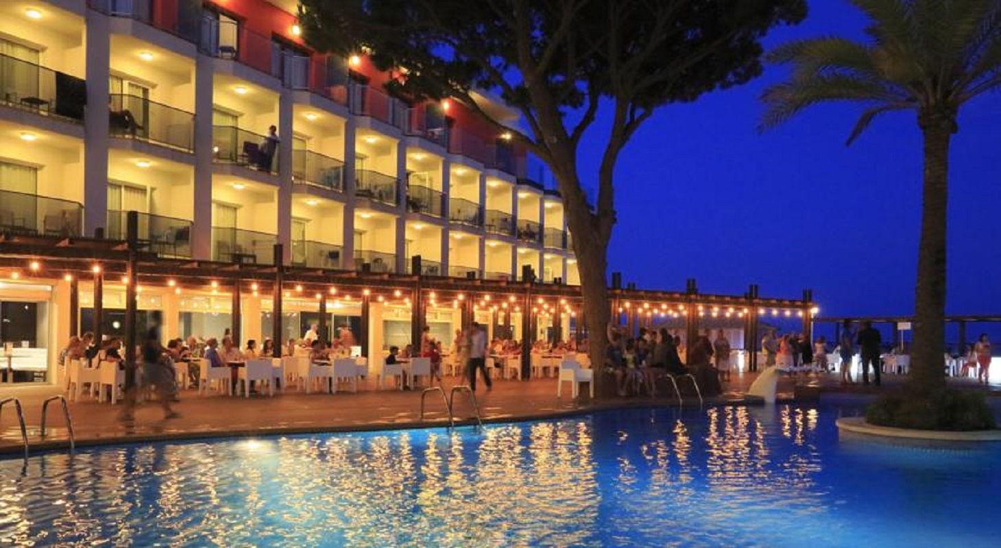 A hotel with a pool, outdoor seating, and a multi-story building with balconies.