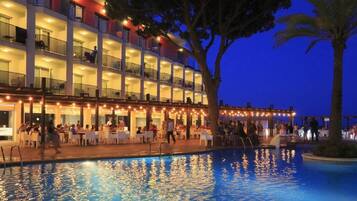 A hotel with a pool, outdoor seating, and a multi-story building with balconies.