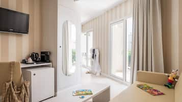 Habitación de hotel con televisor de pantalla plana, cafetera, sofá, zona de juegos para niños y un amplio ventanal con cortinas.