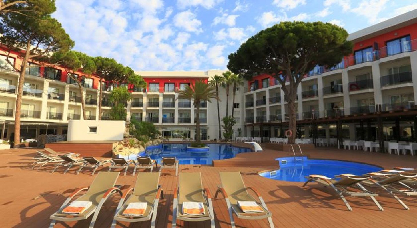 A hotel with a central swimming pool surrounded by lounge chairs and a multi-story building with balconies.