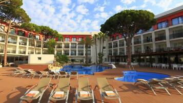 A hotel with a central swimming pool surrounded by lounge chairs and a multi-story building with balconies.