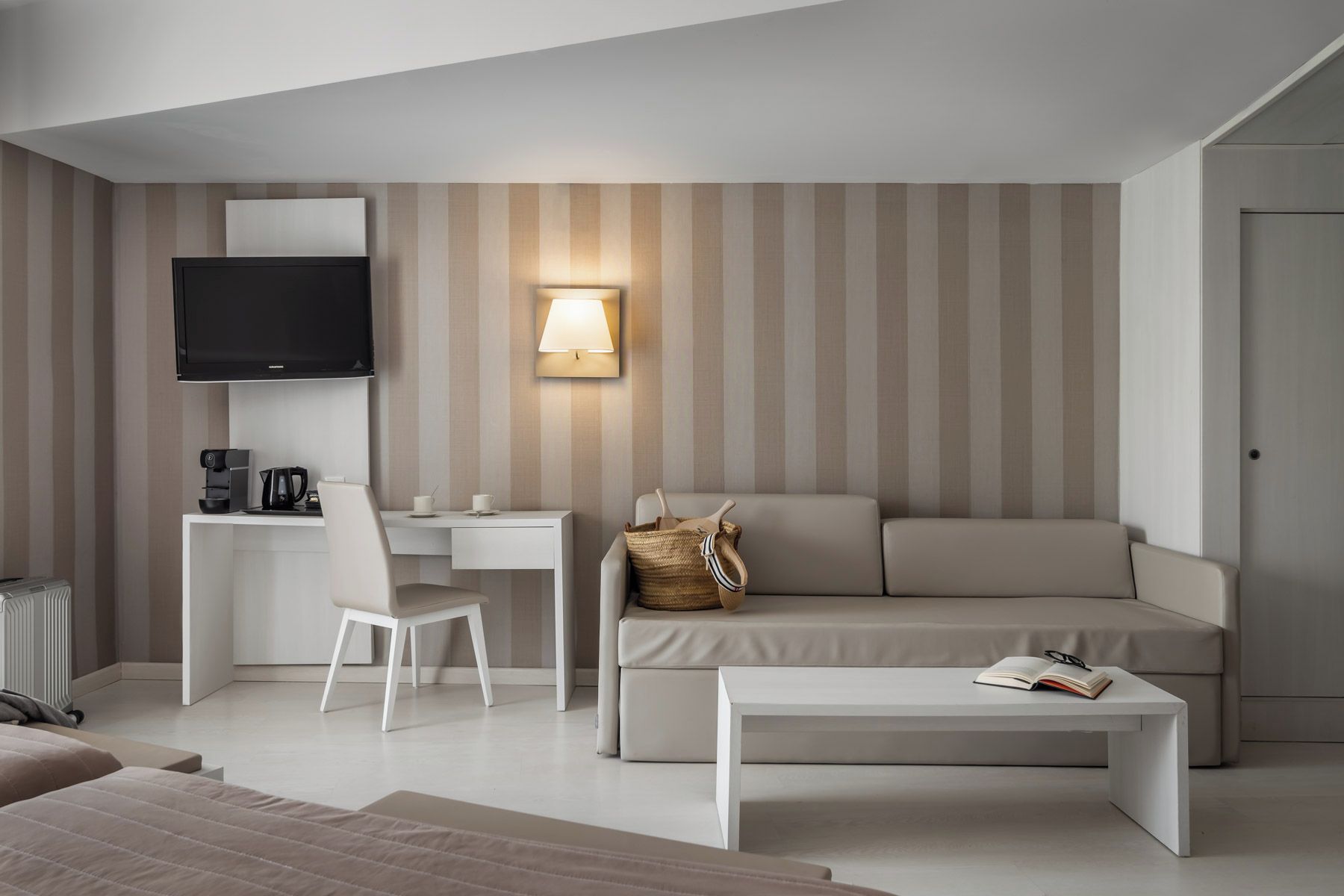 Habitación de hotel moderna con una televisión de pantalla plana, un escritorio con una silla, un sofá, una mesa de centro y una lámpara de pared.