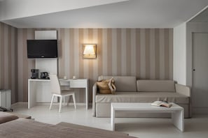 A modern hotel room with a flat-screen TV, a desk with a chair, a sofa, a coffee table, and a wall-mounted lamp. - Estival Centurión (Cambrils)