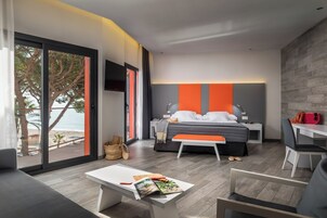 Quarto moderno com cama, mesas de cabeceira, um banco e vista para a praia.