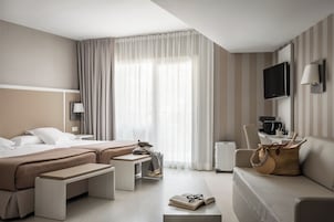 Una habitación de hotel con cama, dos mesitas de noche, sofá, televisor y cafetera.