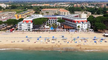 A coastal hotel with multiple floors, a beach in the foreground, and a view of the cityscape in the background.